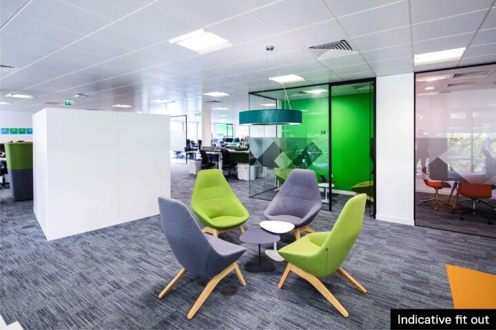Modern office lounge area with four chairs around small tables, near glass-walled meeting room.