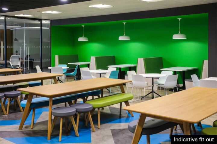 Modern office break area with green accent wall, wooden tables, benches, and white chairs.