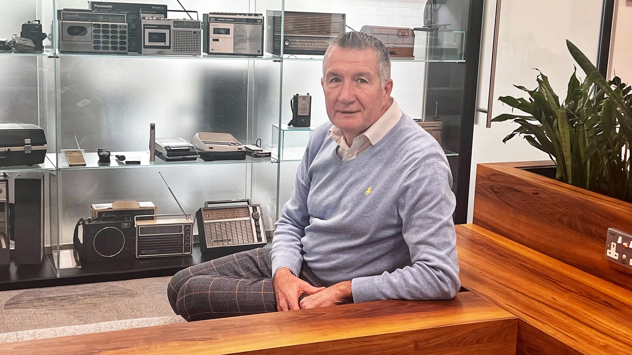 Man sitting on a wooden bench in an office with vintage radios on display behind glass.