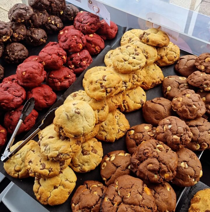 Rows of assorted cookies, including chocolate chip, red velvet, and double chocolate, on display.