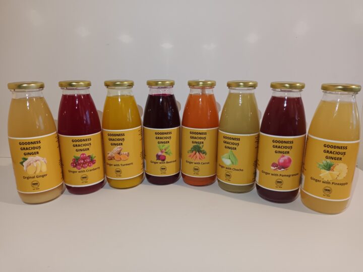 Eight bottles of Goodness Gracious Ginger drinks in various flavors are lined up against a white background.