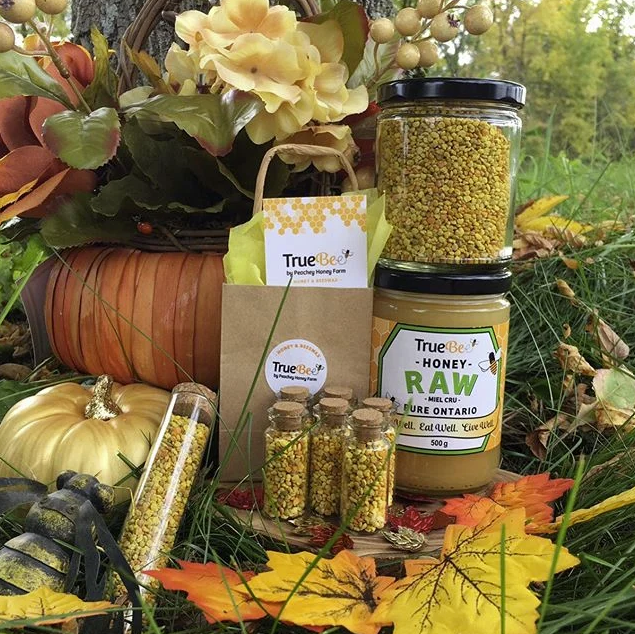 Various TrueBee honey and bee pollen products arranged outdoors among autumn leaves and decorations.