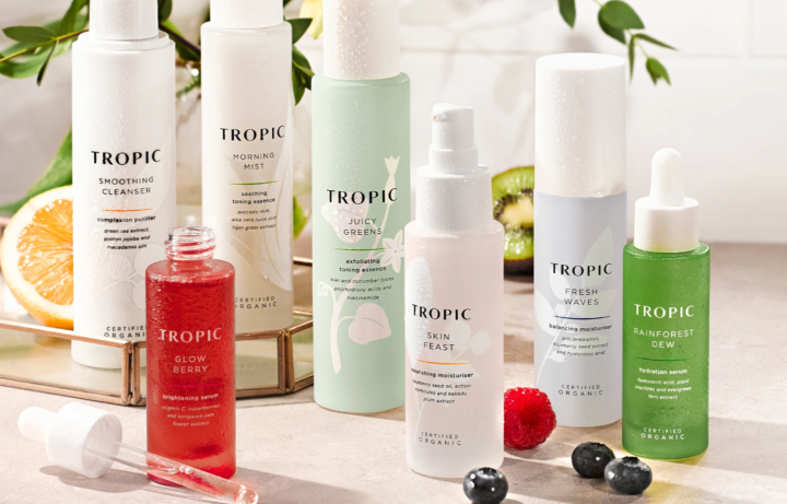 Several Tropic skincare products are arranged on a counter with fruit slices and berries nearby.